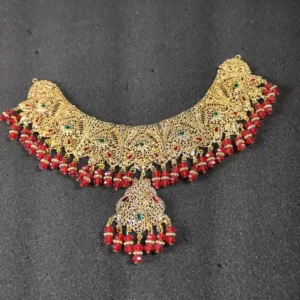 Elegant gold-tone women's jewelry set, including a captivating step necklace, Maang Tika, Earrings and Nose Ring adorned with vibrant red beads for a touch of sophistication and style