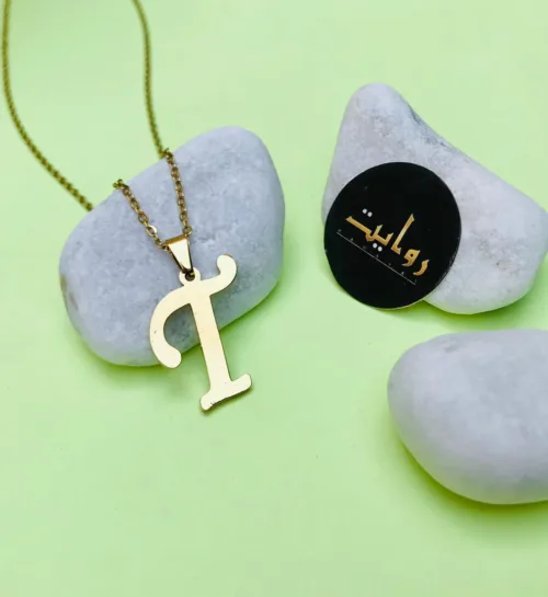 capital letter 'T' pendant. The pendant, intricately designed with filigree details, hangs elegantly from a slender chain, adding a touch of sophistication and personalization to the accessory.